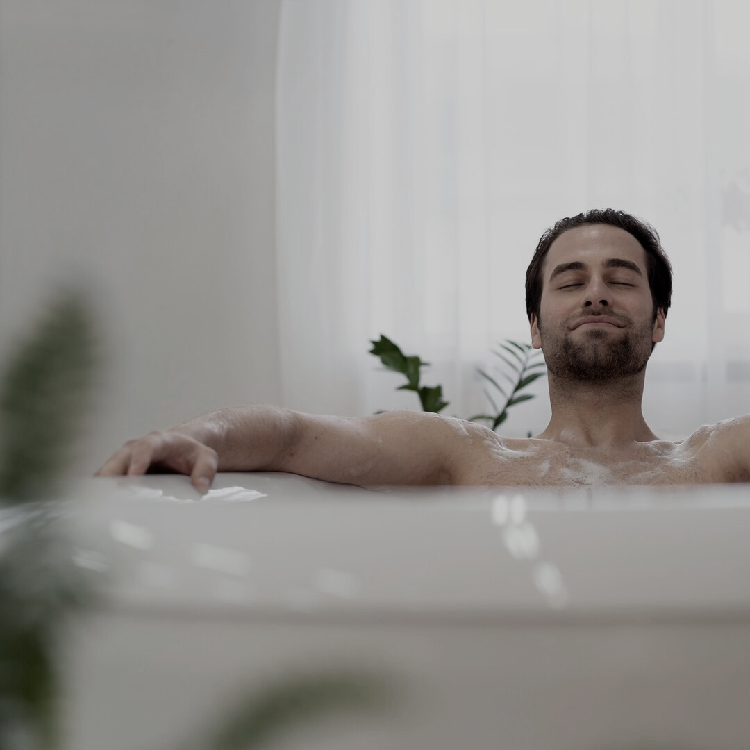 Man relaxing in a bathtub with eyes closed, surrounded by soft lighting.